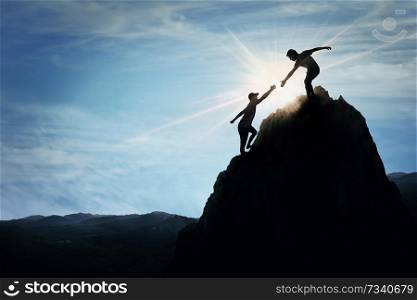 Silhouette of helping hand between two boys climbing a rocky dangerous cliff. Friendly hand on the high mountain hike. Inspirational teamwork, faith and support symbol.