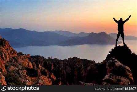 silhouette of hiker enjoying at the top of cliff overlooking the sea in front of a beautiful sky at sunset