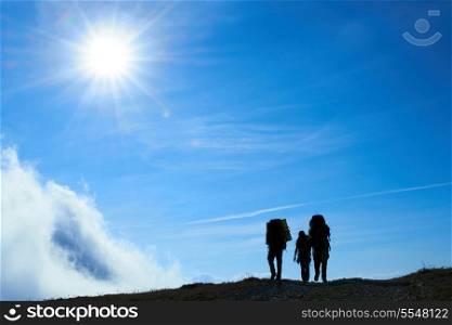 Silhouette of hiking friends against sun and blue sky