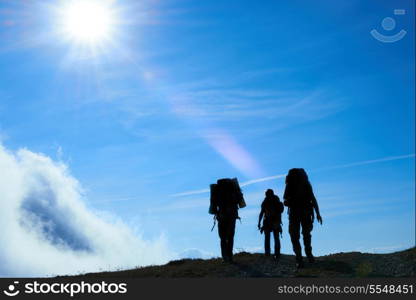 Silhouette of hiking friends against sun and blue sky