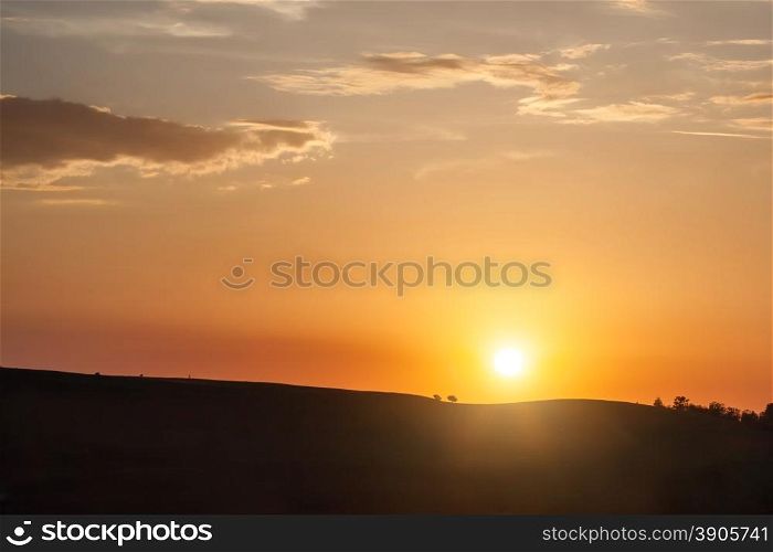 Silhouette of hill on sunset with sun and clouds