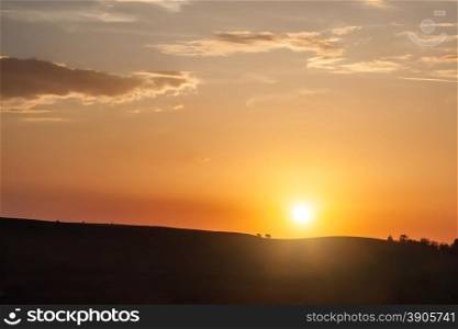 Silhouette of hill on sunset with sun and clouds