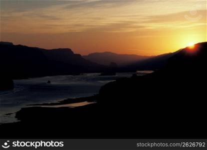 Silhouette of hills and river with sunset in background