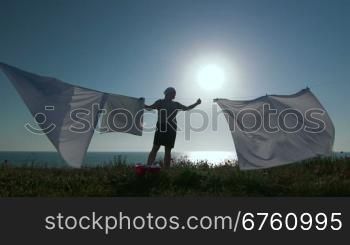 Silhouette of housewife and white laundry on a clothesline against sun