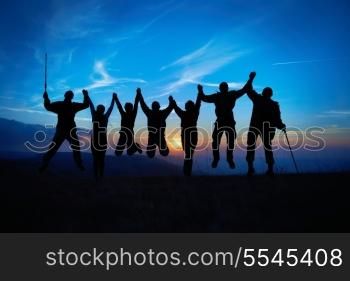 Silhouette of jumping friends in sunset against blue sky