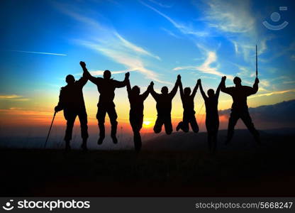 Silhouette of jumping friends in sunset against blue sky