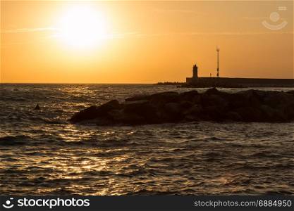 Silhouette of Lighthouse, Reef, and Choppy Sea at Sunset