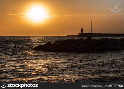 Silhouette of Lighthouse, Reef, and Choppy Sea at Sunset