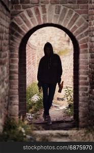 Silhouette of Lonely Teenager Girl Standing in the Brick Ruins and Drinking Beer in a Sweatshirt with a Hood