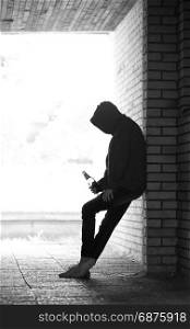 Silhouette of Lonely Teenager Standing in the Dark Doorway with Beer Bottle in a Sweatshirt with a Hood