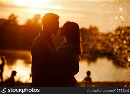 silhouette of loving couple hugging on the lake at sunset. Beautiful young couple in love walking on the shore of the lake at sunset in the rays of bright light. copy space. selective focus.. silhouette of loving couple hugging on the lake at sunset. Beautiful young couple in love walking on the shore of the lake at sunset in the rays of bright light. copy space. selective focus