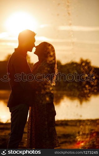 silhouette of loving couple hugging on the lake at sunset. Beautiful young couple in love walking on the shore of the lake at sunset in the rays of bright light. copy space. selective focus.. silhouette of loving couple hugging on the lake at sunset. Beautiful young couple in love walking on the shore of the lake at sunset in the rays of bright light. copy space. selective focus