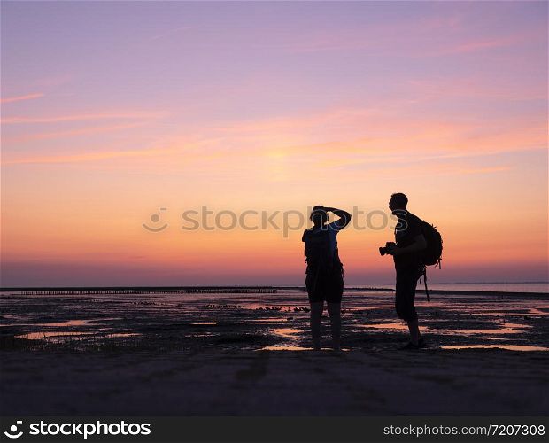 silhouette of man and woman taking pictures with camera of colorful sunset