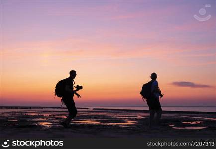 silhouette of man and woman taking pictures with camera of colorful sunset