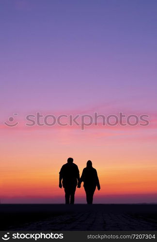 silhouette of man and woman walk holding hands in colorful sunset