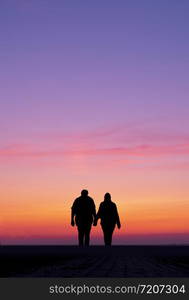 silhouette of man and woman walk holding hands in colorful sunset