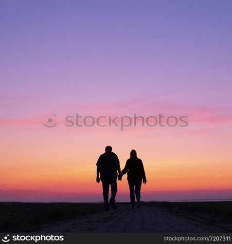 silhouette of man and woman walk towards colorful sunset holding hands