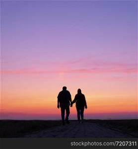 silhouette of man and woman walk towards colorful sunset holding hands