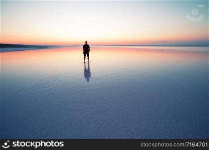 Silhouette of man departing into sunset on smooth water of lake. The concept of privacy and harmony. Silhouette of man departing into sunset on smooth water of lake