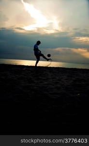 silhouette of man playing soccer on the beach