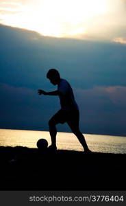 silhouette of man playing soccer on the beach