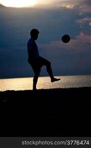 silhouette of man playing soccer on the beach