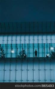 Silhouette of man standing on backlit glass construction in a city center at night