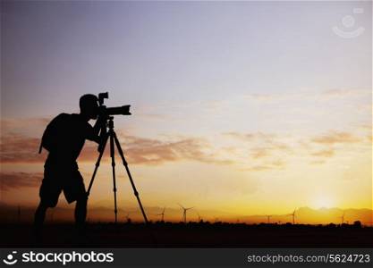 Silhouette of man taking photos with his camera at sunset with a dramatic sky