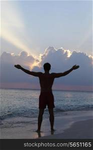 Silhouette Of Man With Outstretched Arms On Beach At Sunset
