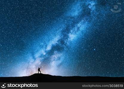 Silhouette of man with trekking poles against amazing Milky Way at night. Space background. Landscape with man on the hill, bright milky way, sky with stars. Beautiful galaxy. Travel. Blue starry sky. Man with trekking poles and sky with Milky Way
