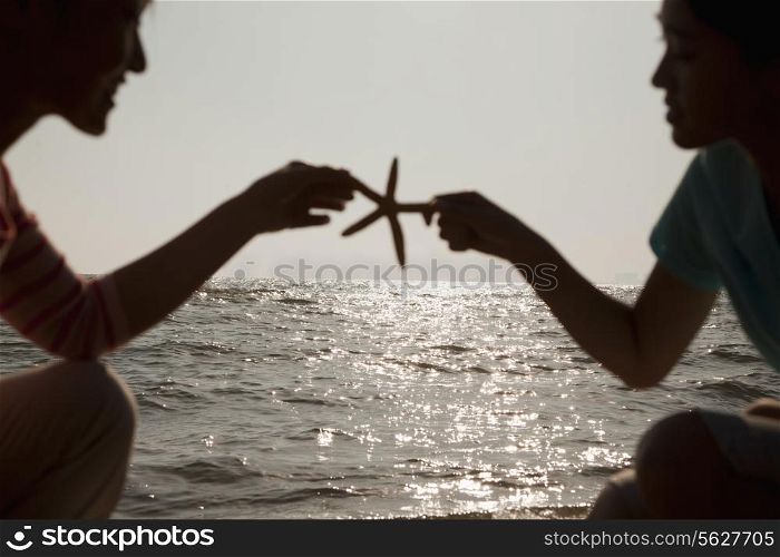 Silhouette of mother and daughter holding a starfish on the beach