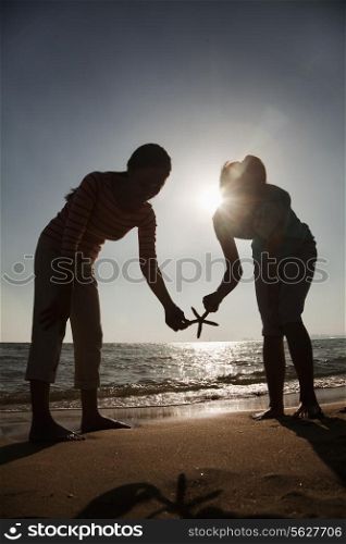 Silhouette of mother and daughter holding a starfish on the beach