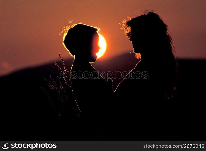 Silhouette of mother and son talking with sun and sunset in background