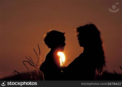 Silhouette of mother and son talking with sun and sunset in background
