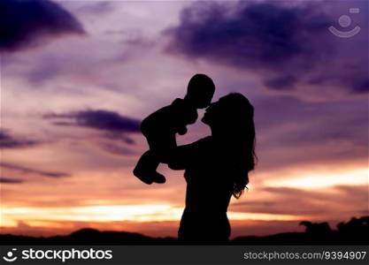 silhouette of mother holding and kissing with her infant baby at sunset