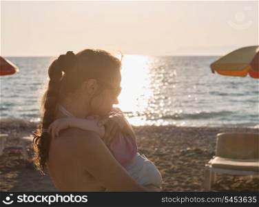 Silhouette of mother hugging baby on lonely beach