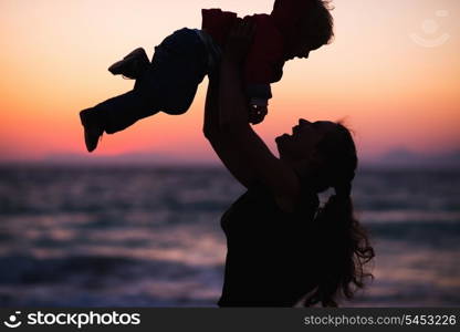 Silhouette of mother throwing baby up on sunset