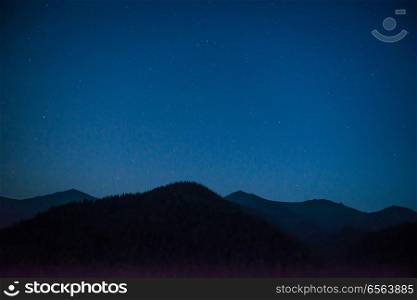 Silhouette of mountain range under dark blue night sky with many bright stars. Silhouette of mountain range at night