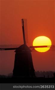 Silhouette of old-fashioned, wooden windmill with yellow setting sun in background