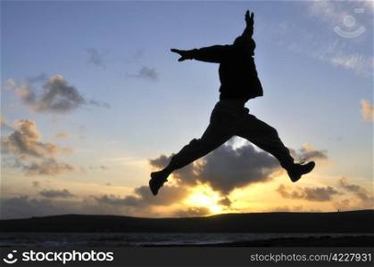 Silhouette of one man jumping over water at the beach.