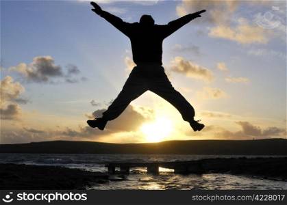Silhouette of one man jumping over water at the beach.