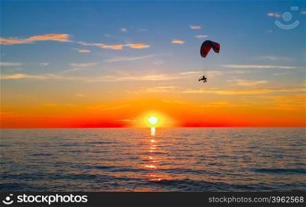Silhouette of paraglider flying over sea at sunset. Sunset at sea and paraglider