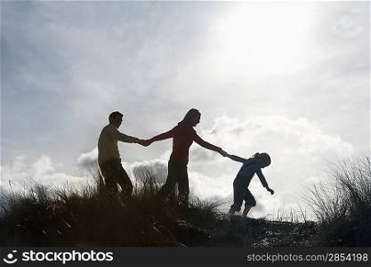 Silhouette of parents and daughter (5-6) holding hands on sand dunes