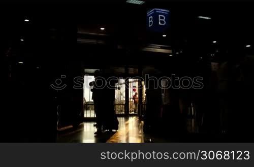 Silhouette of passengers in the airport carrying bags and luggage trolleys in the early morning with back lit sun rays going through the window