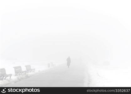 Silhouette of person walking in a foggy winter park