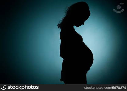 silhouette of pregnant young lady in studio. green background