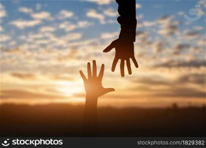 Silhouette of reaching, giving a helping hand, hope and support each other over sunset background. Help concept