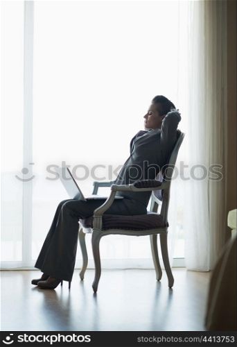 Silhouette of relaxed business woman sitting in hotel room with laptop
