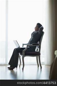 Silhouette of relaxed business woman sitting in hotel room with laptop
