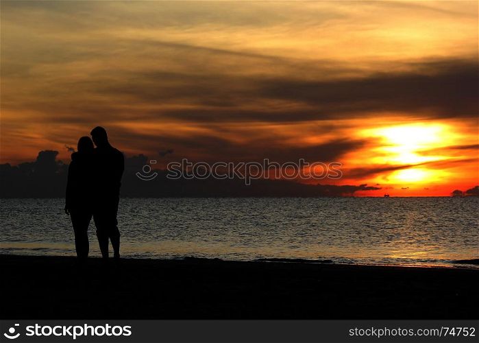 silhouette of romantic honeymoon couple walking on the beach with beautiful sunrise background